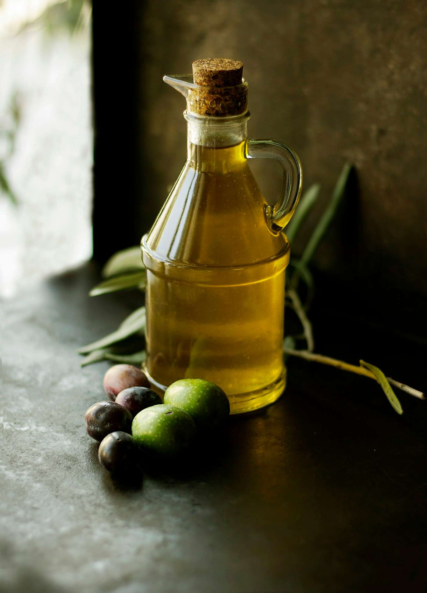 Aceitera de cristal con aceite de oliva junto a unas aceitunas